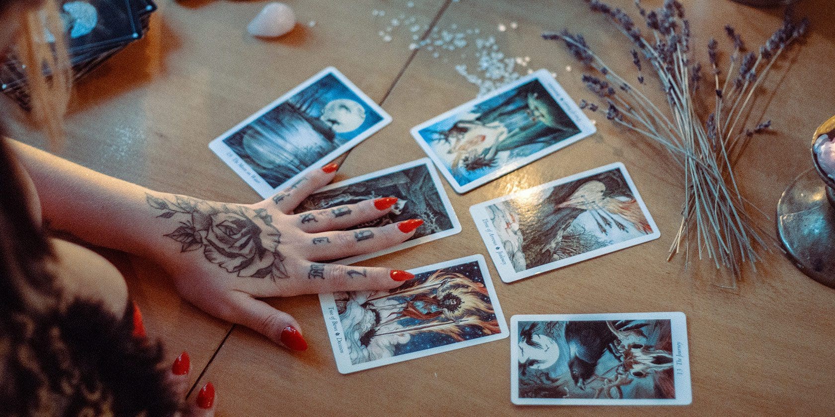 A person with tattoos on their arm is holding onto some tarot cards.